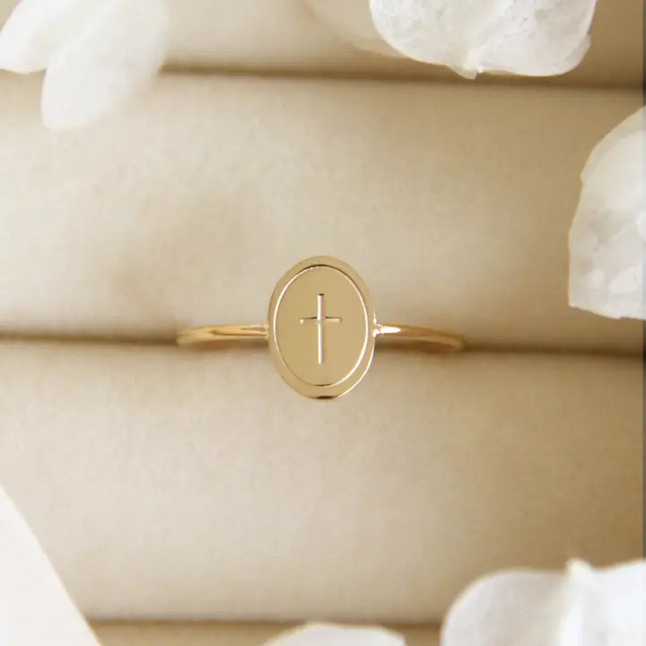 A gold-colored oval cross ring with engraved details, displayed on a pale background.