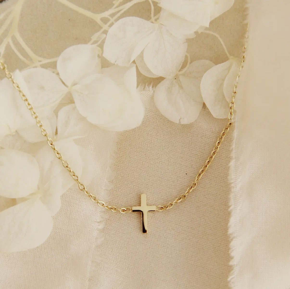 Gold necklace with a cross pendant on a beige floral background